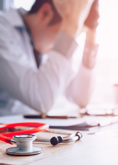 Médecin assis à son bureau qui se tient la tête entre les mains