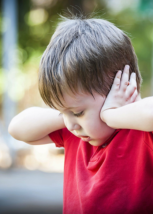 Petit garçon autiste en extérieur , couvrant ses oreilles de ses mains