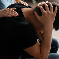 Homme se tenant la tête entre les mains qui se fait réconforter