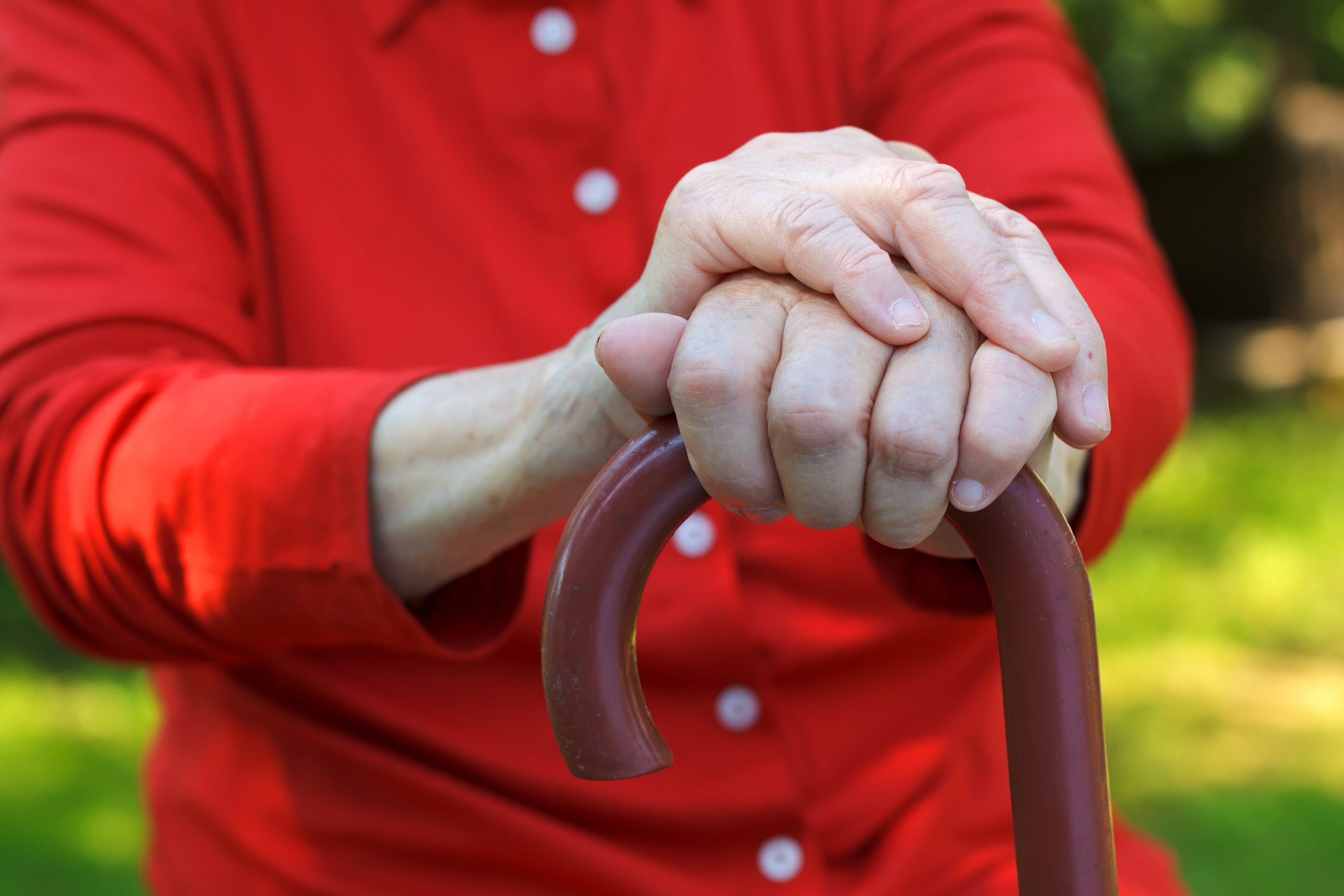 Gros plan sur les mains d’une personne âgée appuyées sur une canne, illustrant le vieillissement, l’autonomie et l’accompagnement des seniors.